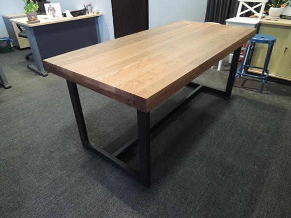 Wooden table with a dark metal frame on a carpeted floor in an office setting.