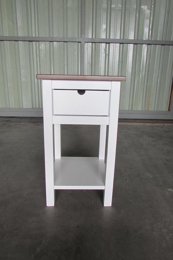 White nightstand with a drawer, shelf, and brown top against a metallic background.