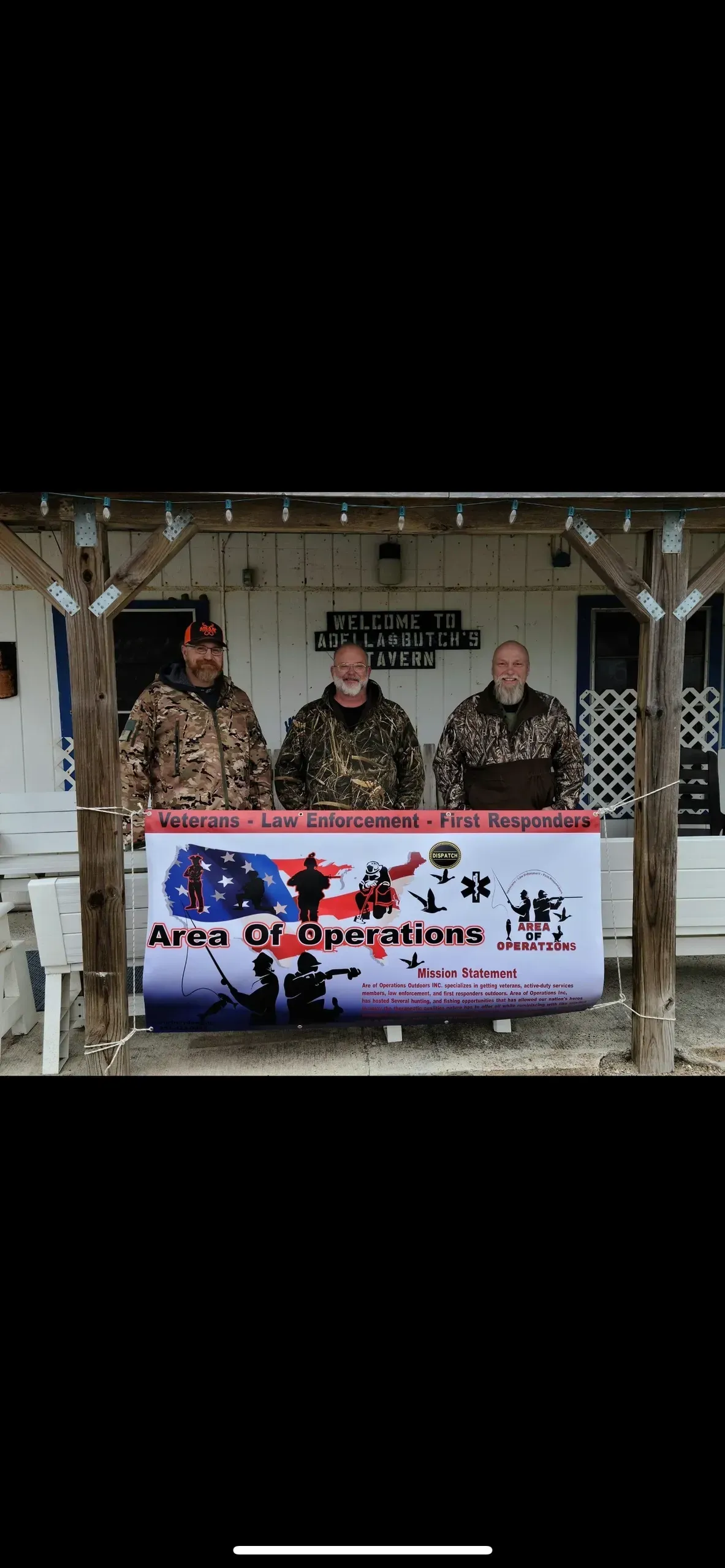 A group of men are standing in front of a sign on a porch.