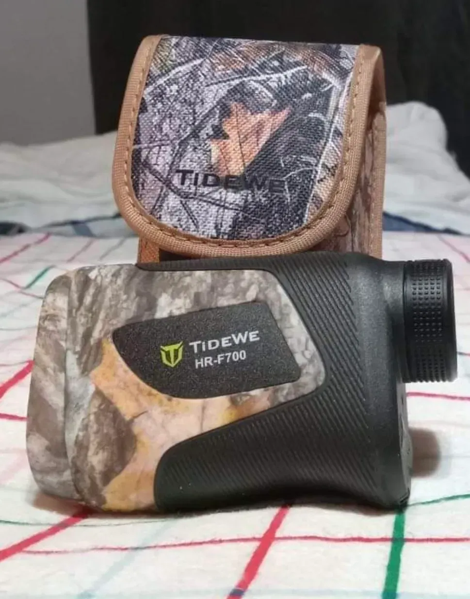 A tidewe rangefinder is sitting on a bed next to its case