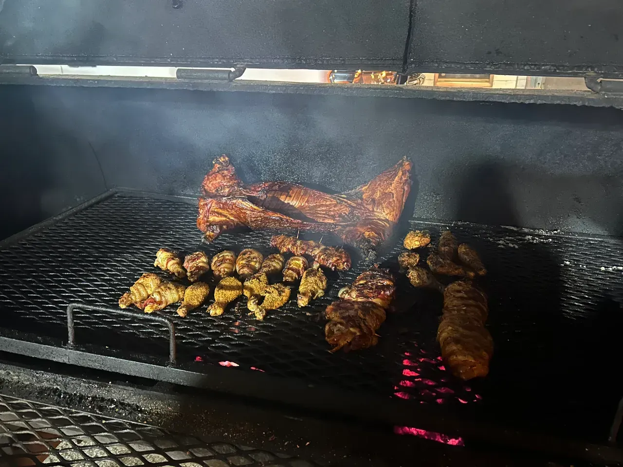 A bunch of meat is cooking on a grill with smoke coming out of it.