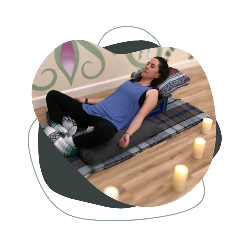 A woman is laying on a yoga mat with her eyes closed surrounded by candles.