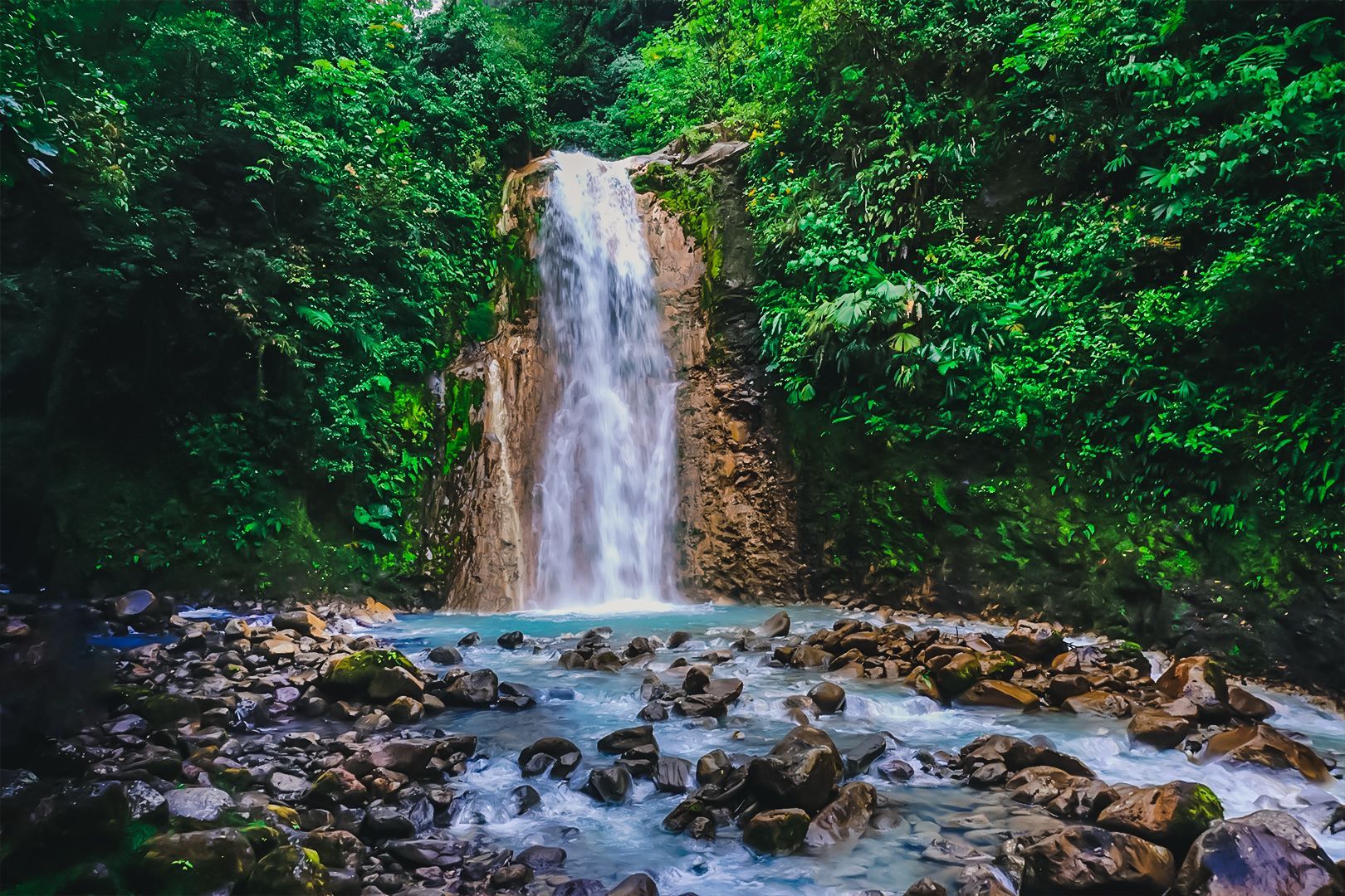 A waterfall in the middle of a lush green forest surrounded by rocks and trees.