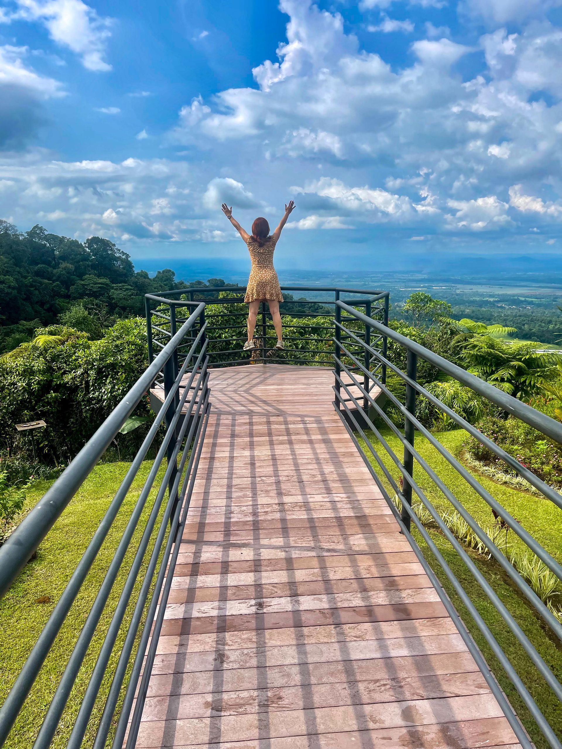 A woman is standing on a bridge with her arms in the air.