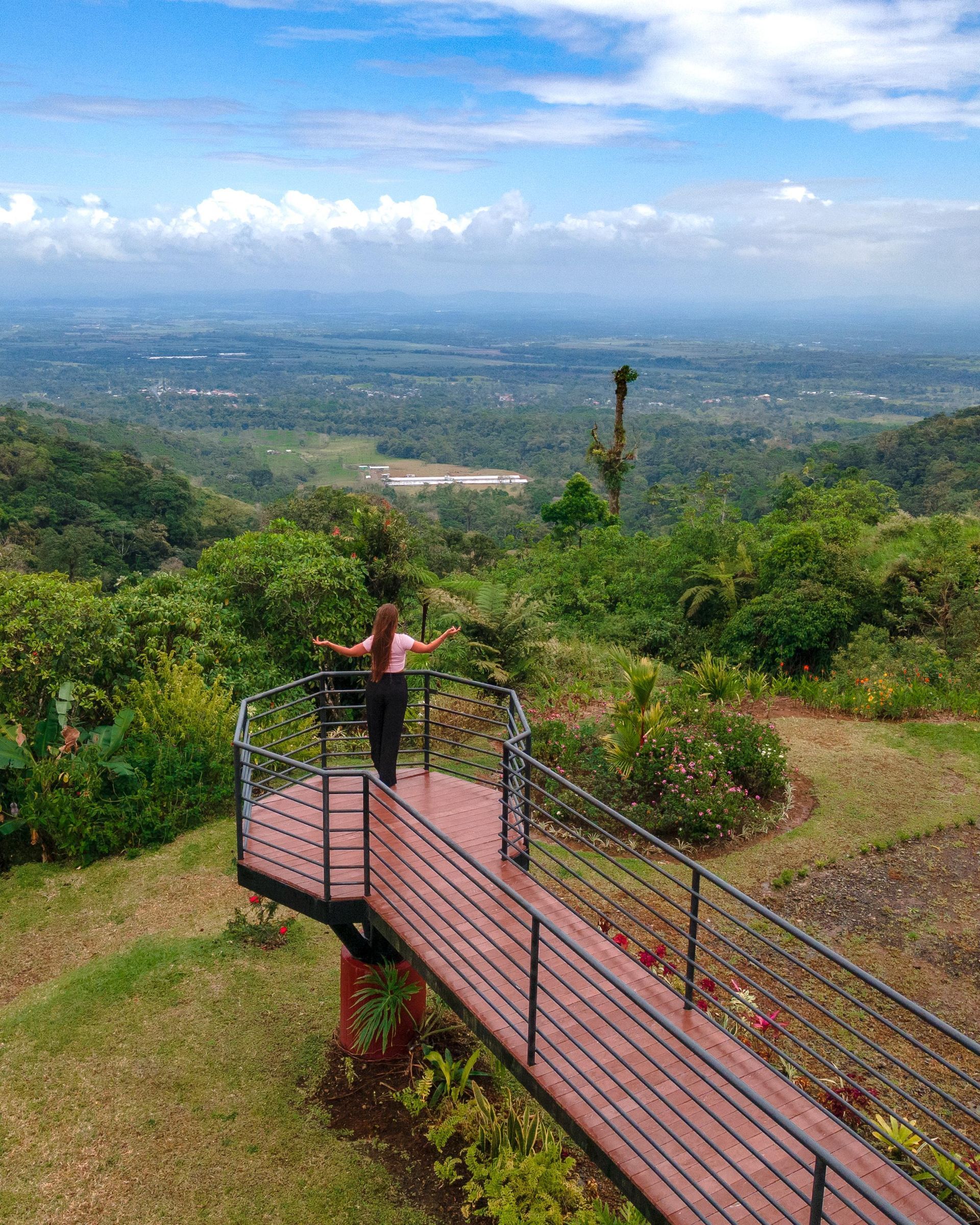 A woman is standing on a wooden deck overlooking a lush green valley.