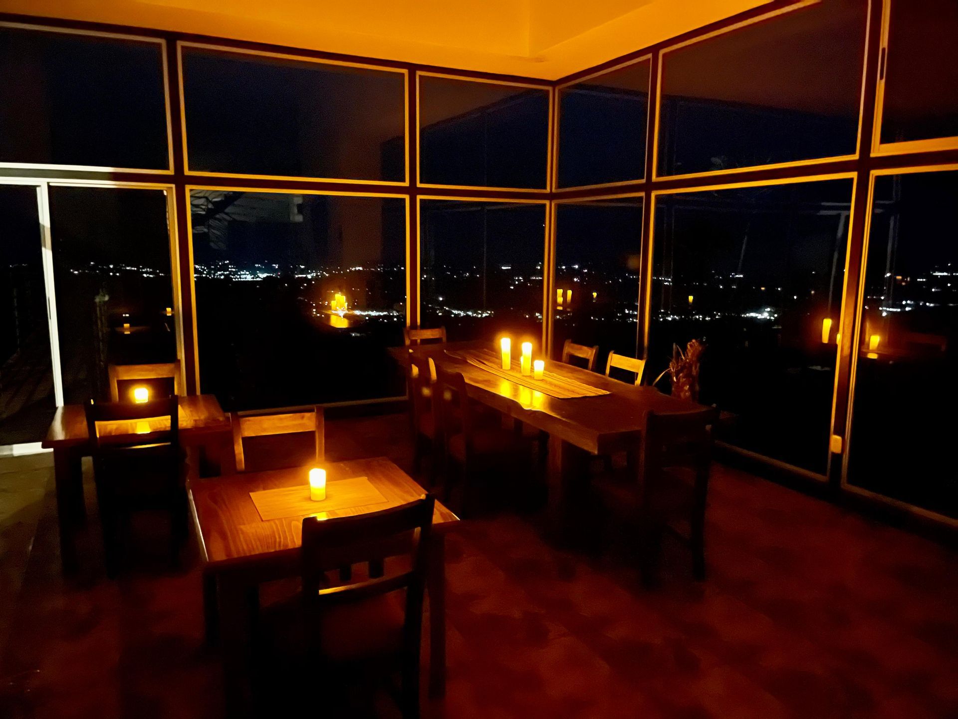 A dining room with a table and chairs and candles lit up at night.
