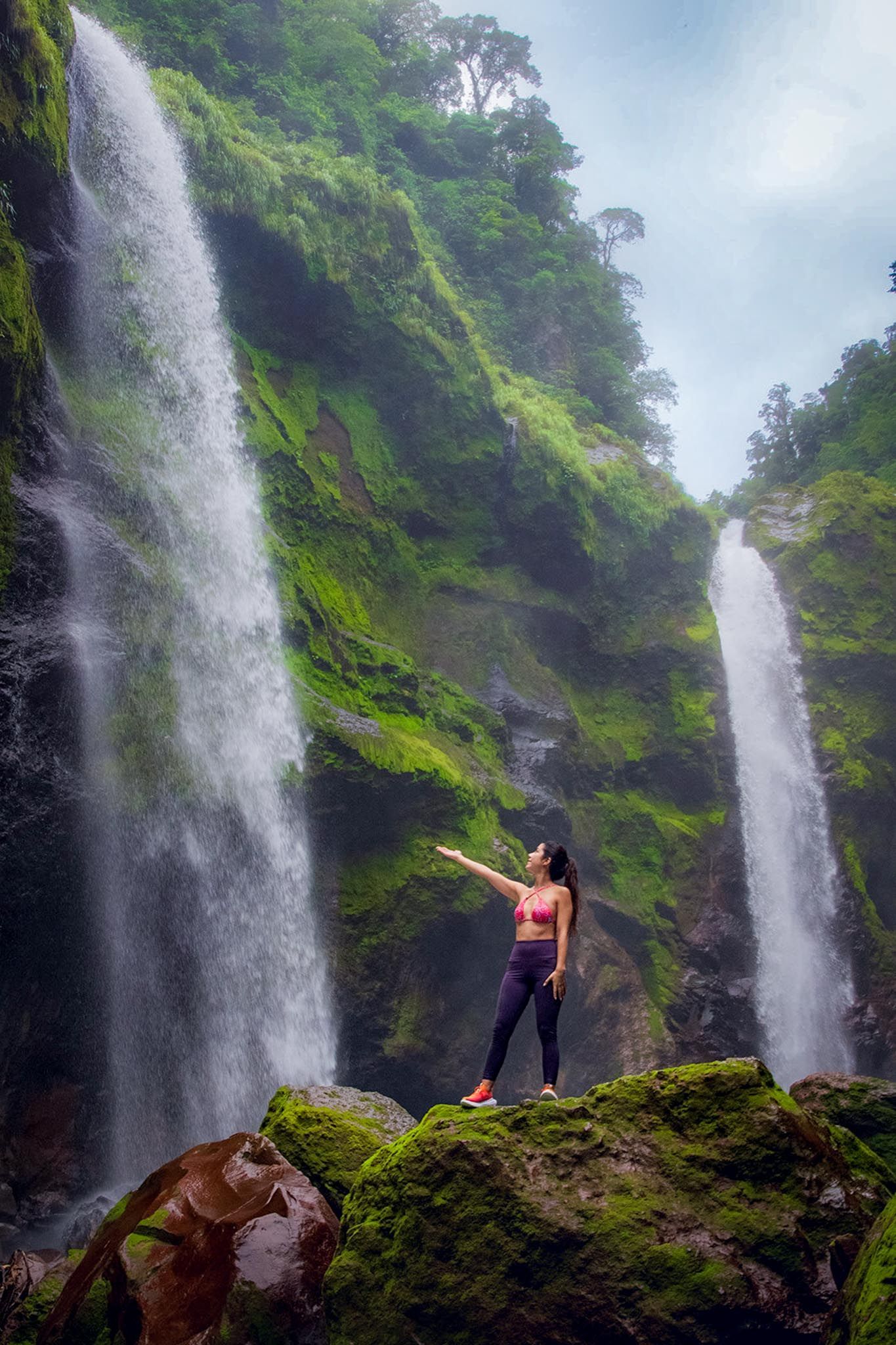 A woman is standing on a rock in front of a waterfall.