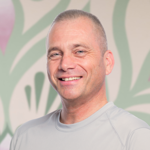 A man in a grey shirt is smiling for the camera.
