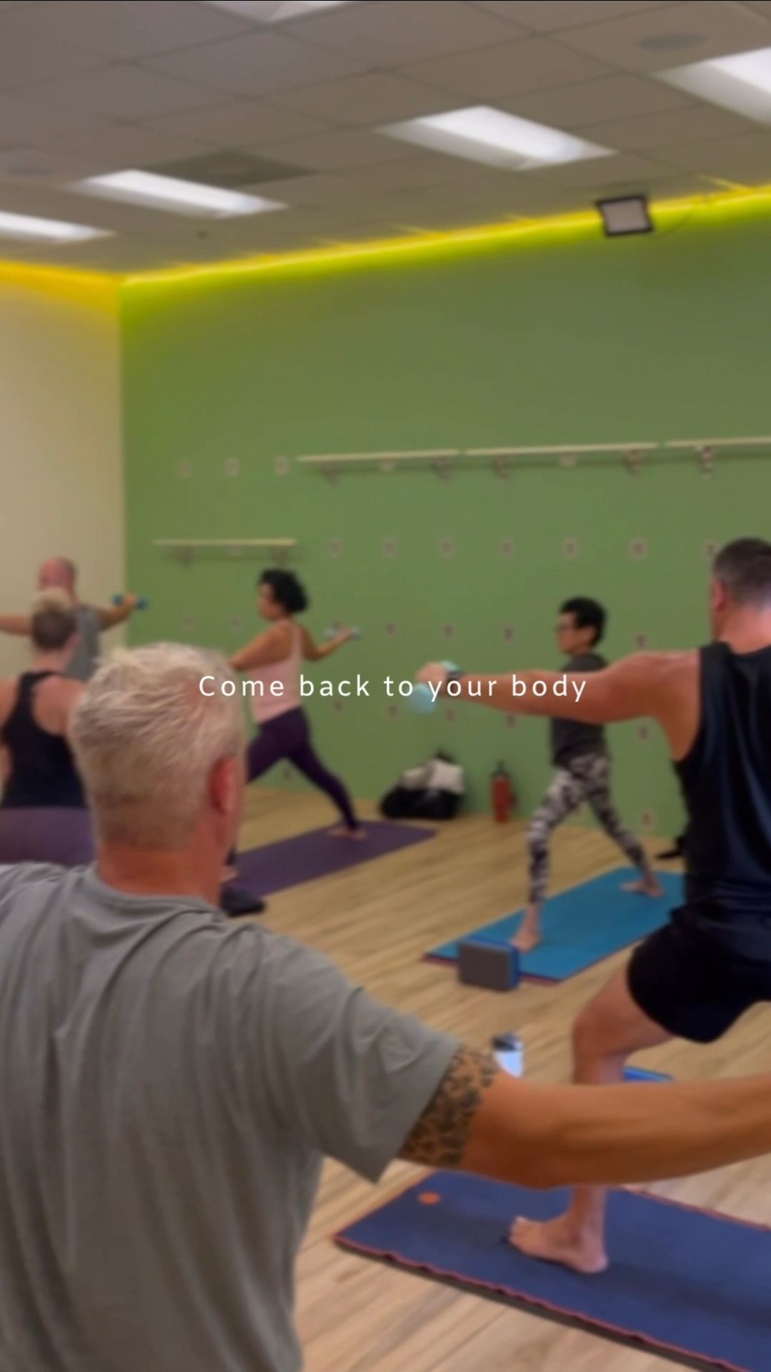An elderly woman is holding a yoga mat in a gym.