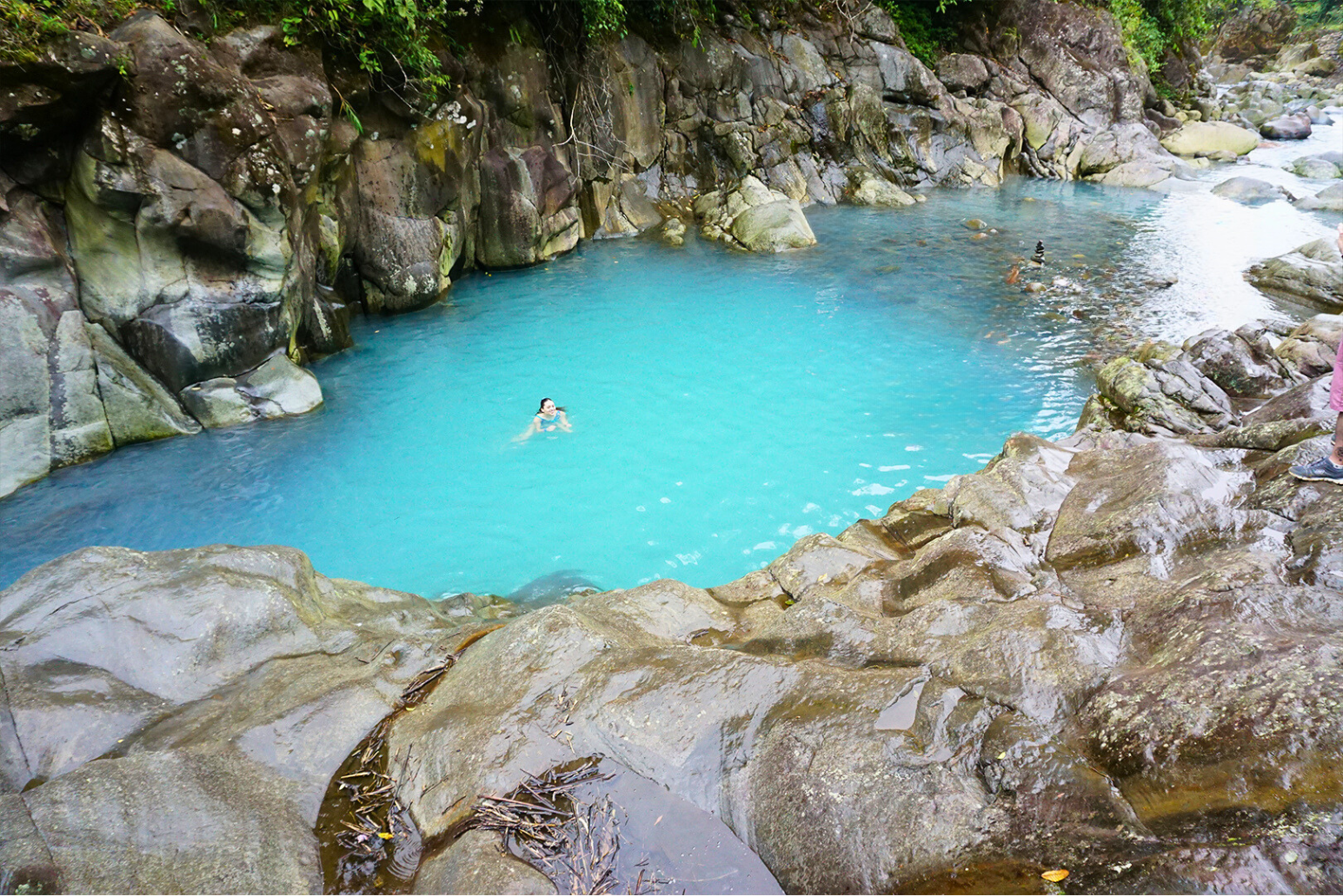 A person is swimming in a pool of blue water surrounded by rocks