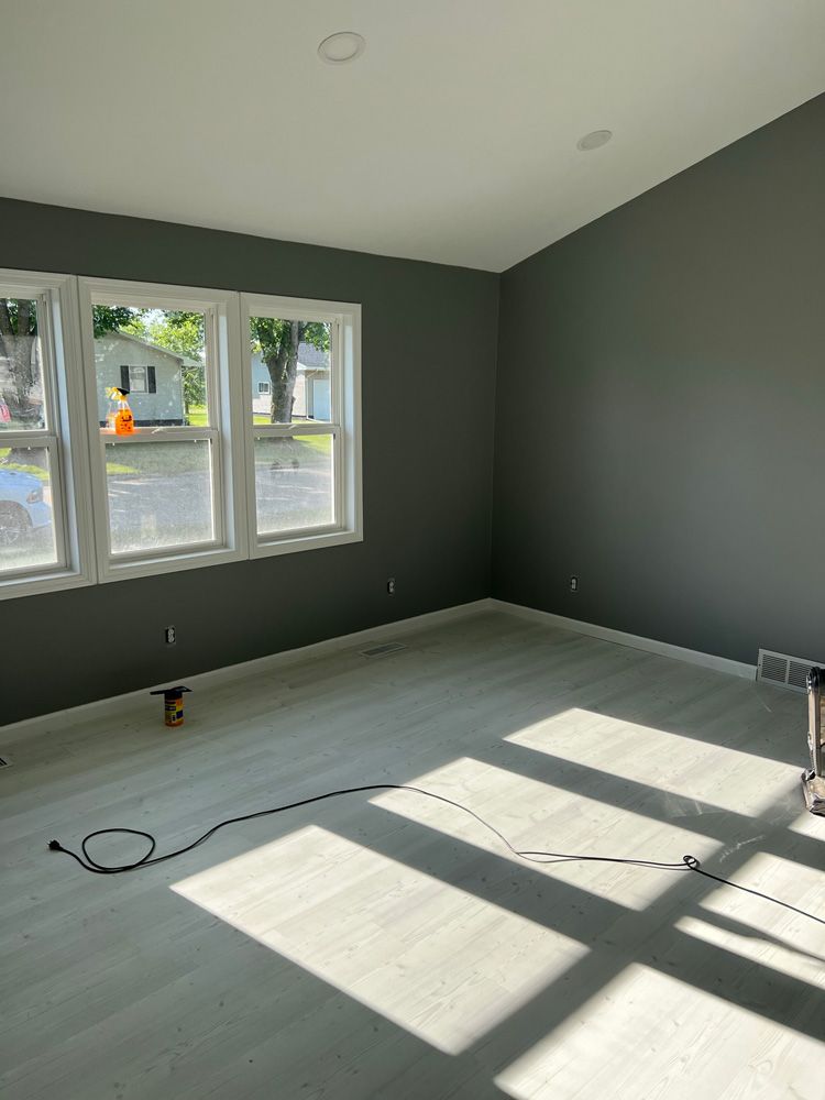 Empty room with gray walls and light gray flooring, with sunlight streaming in through windows.