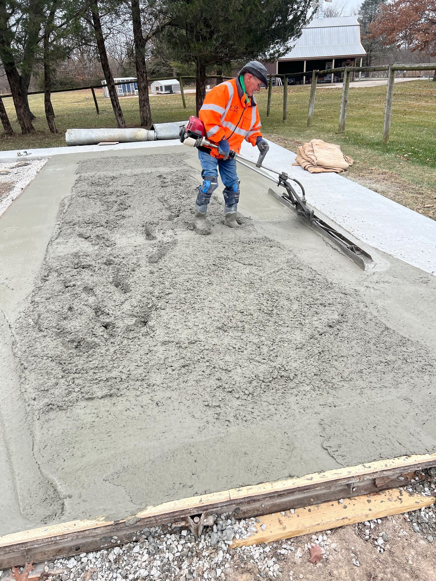 Man in orange vest smoothing wet concrete on a rectangular form outdoors.