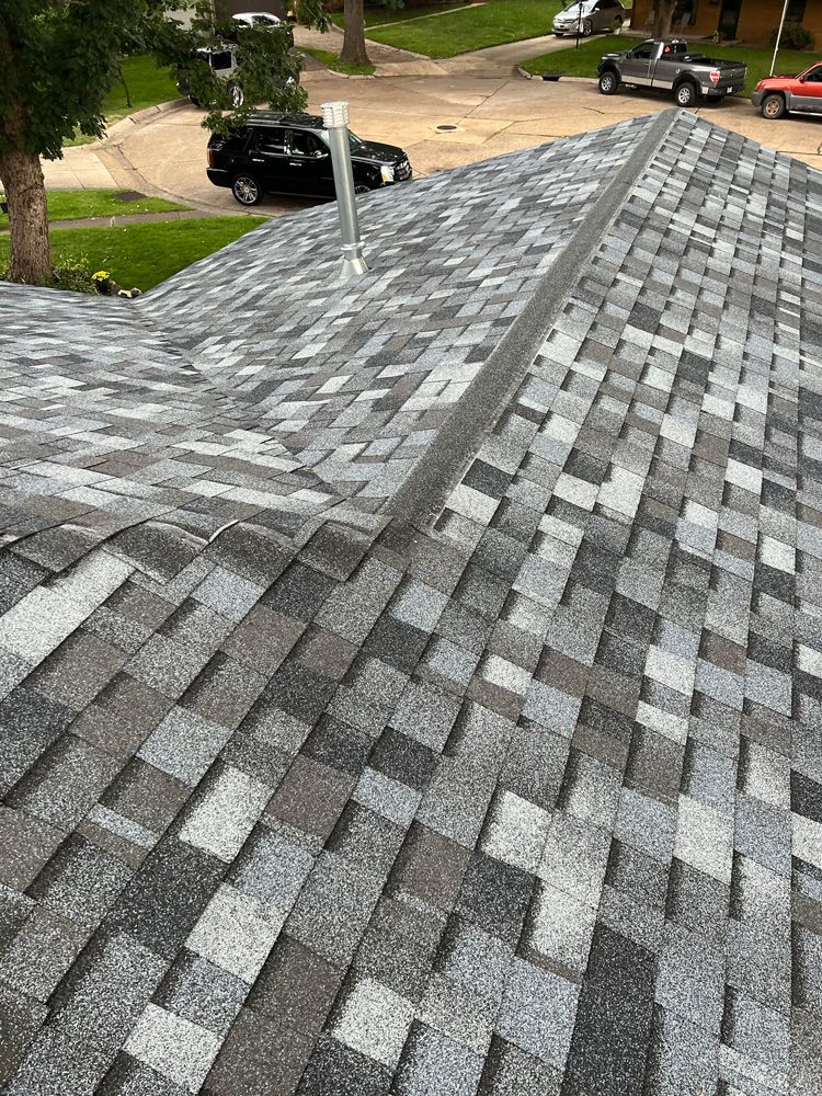 Close-up view of a newly shingled roof with various shades of gray. Cars parked in the background.