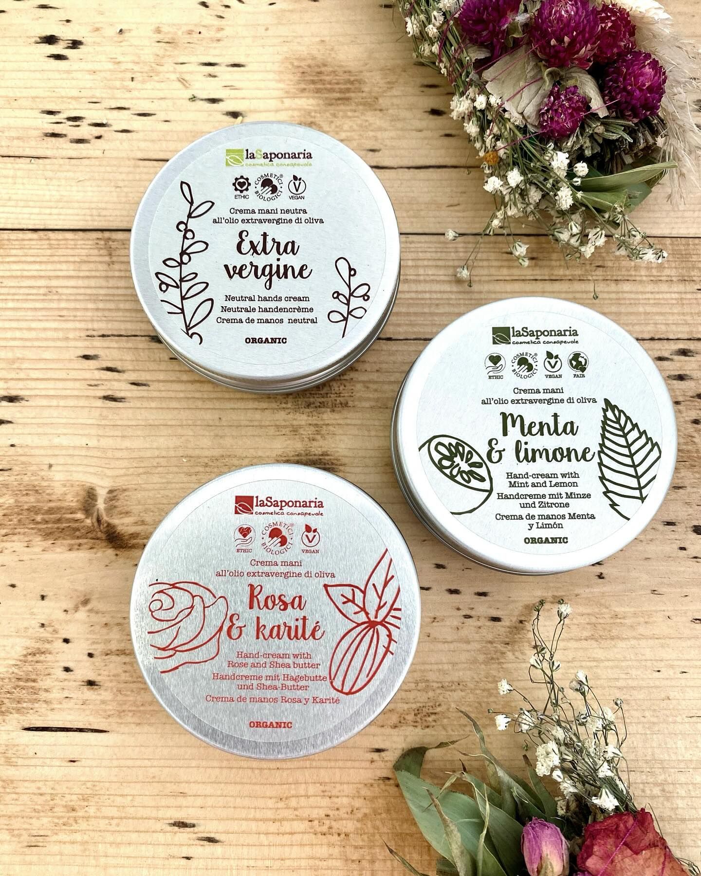 Tre barattoli di sapone sono seduti su un tavolo di legno accanto ai fiori.