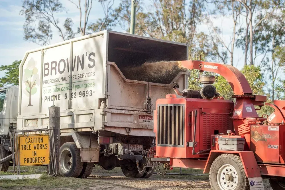 A Wood Chipper Blowing Wood Chips Into the Back of A Truck — Brown's Professional Tree Service In Pie Creek, QLD