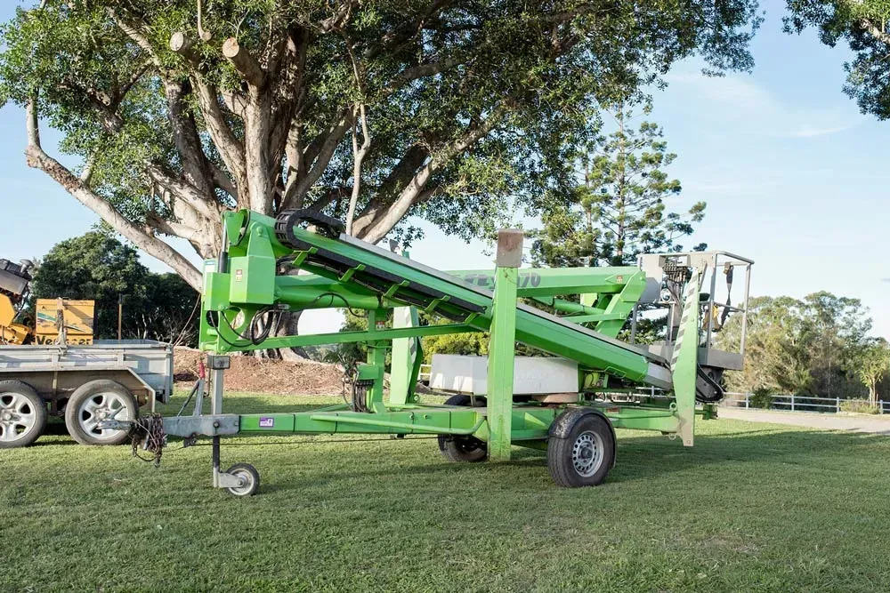 Green Cherry Picker on A Trailer Parked on Grass in Front of A Large Tree — Brown's Professional Tree Service In Pie Creek, QLD