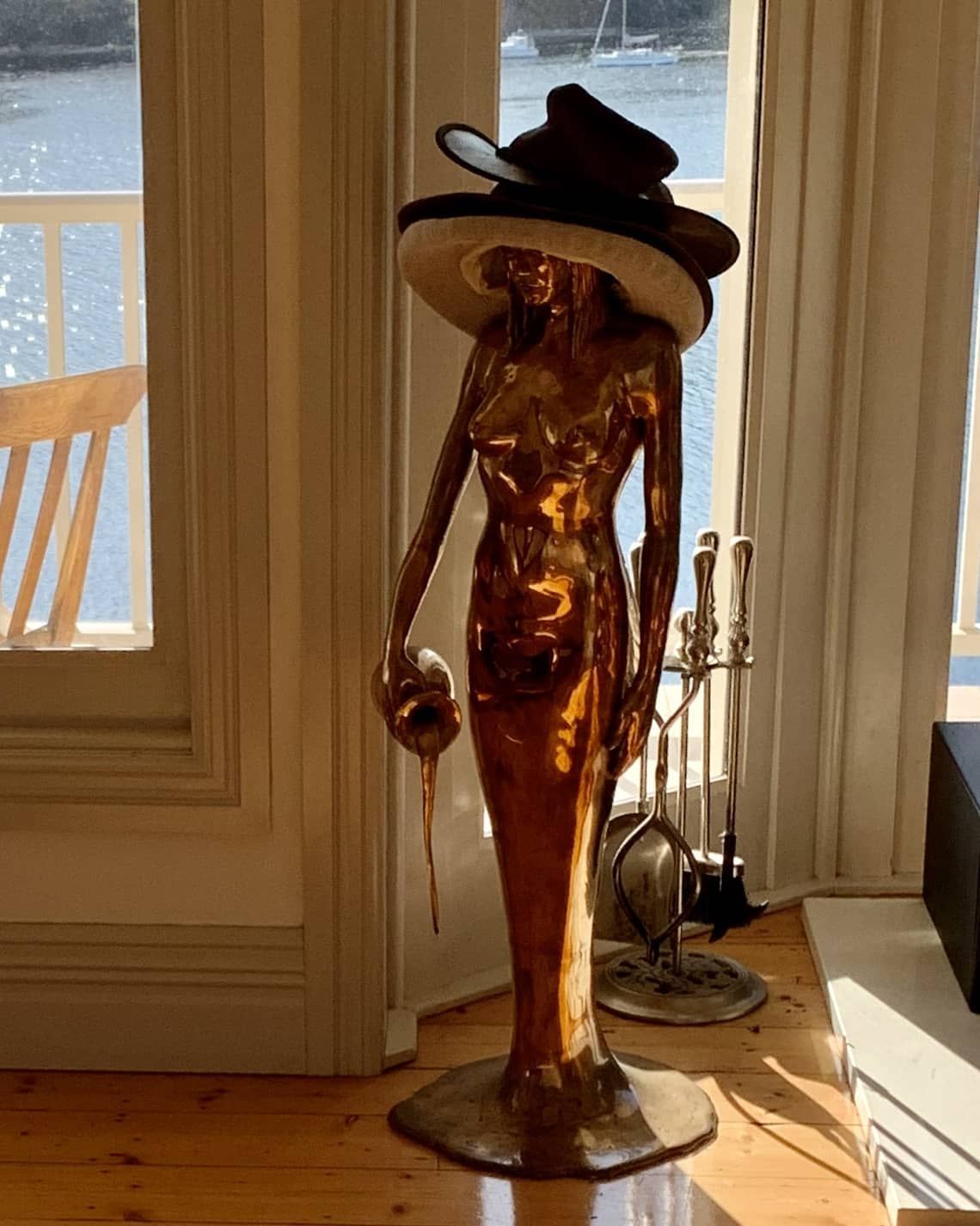 A statue of a woman wearing a hat is standing in front of a window.