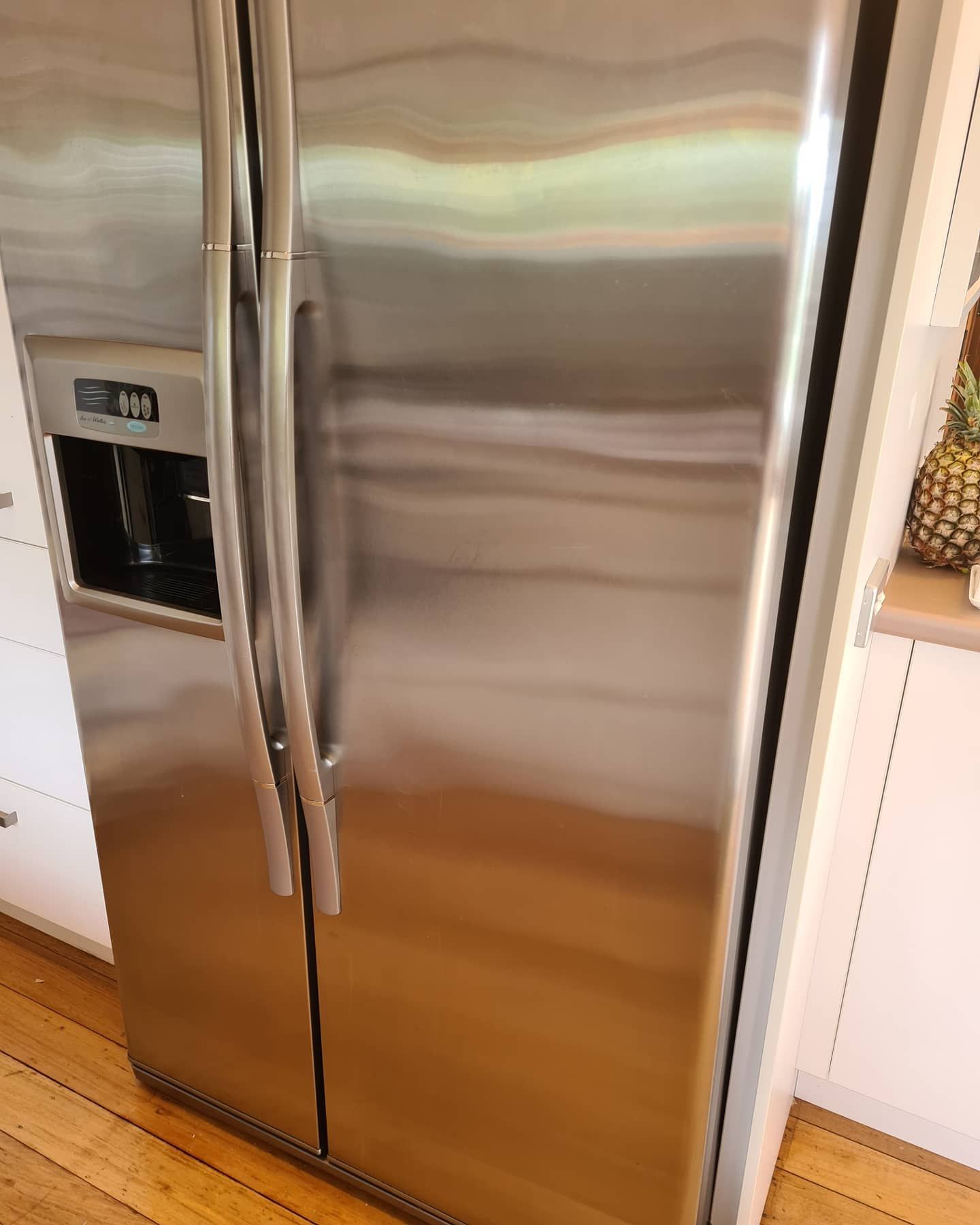 A stainless steel refrigerator is sitting on a wooden floor in a kitchen.