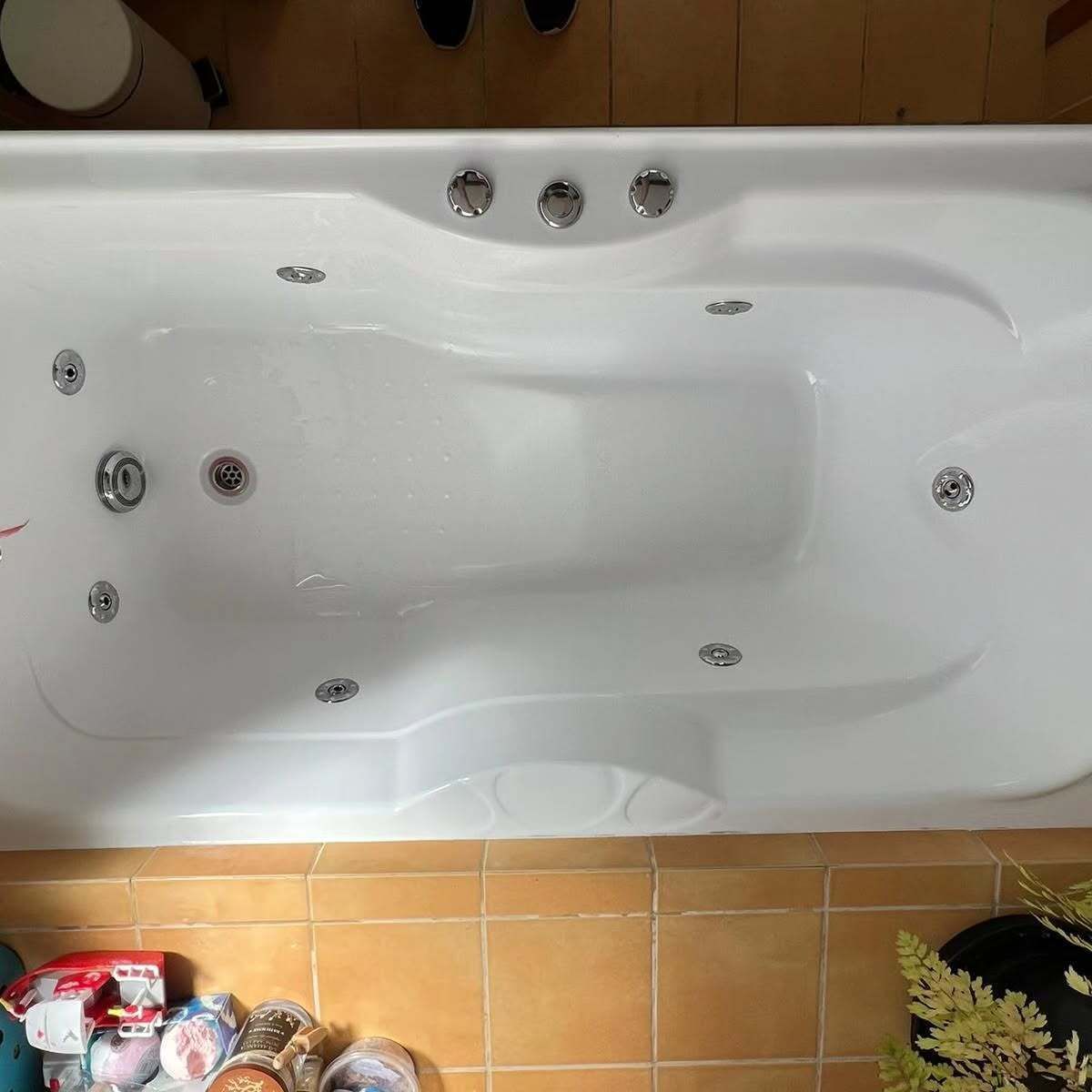 A white bathtub is sitting on a tiled floor next to a plant.