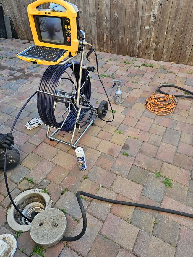 A drain camera is sitting on a brick sidewalk next to a laptop.