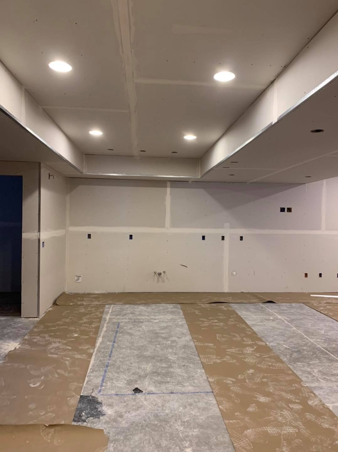 A large room with white walls and a brown floor is being remodeled.