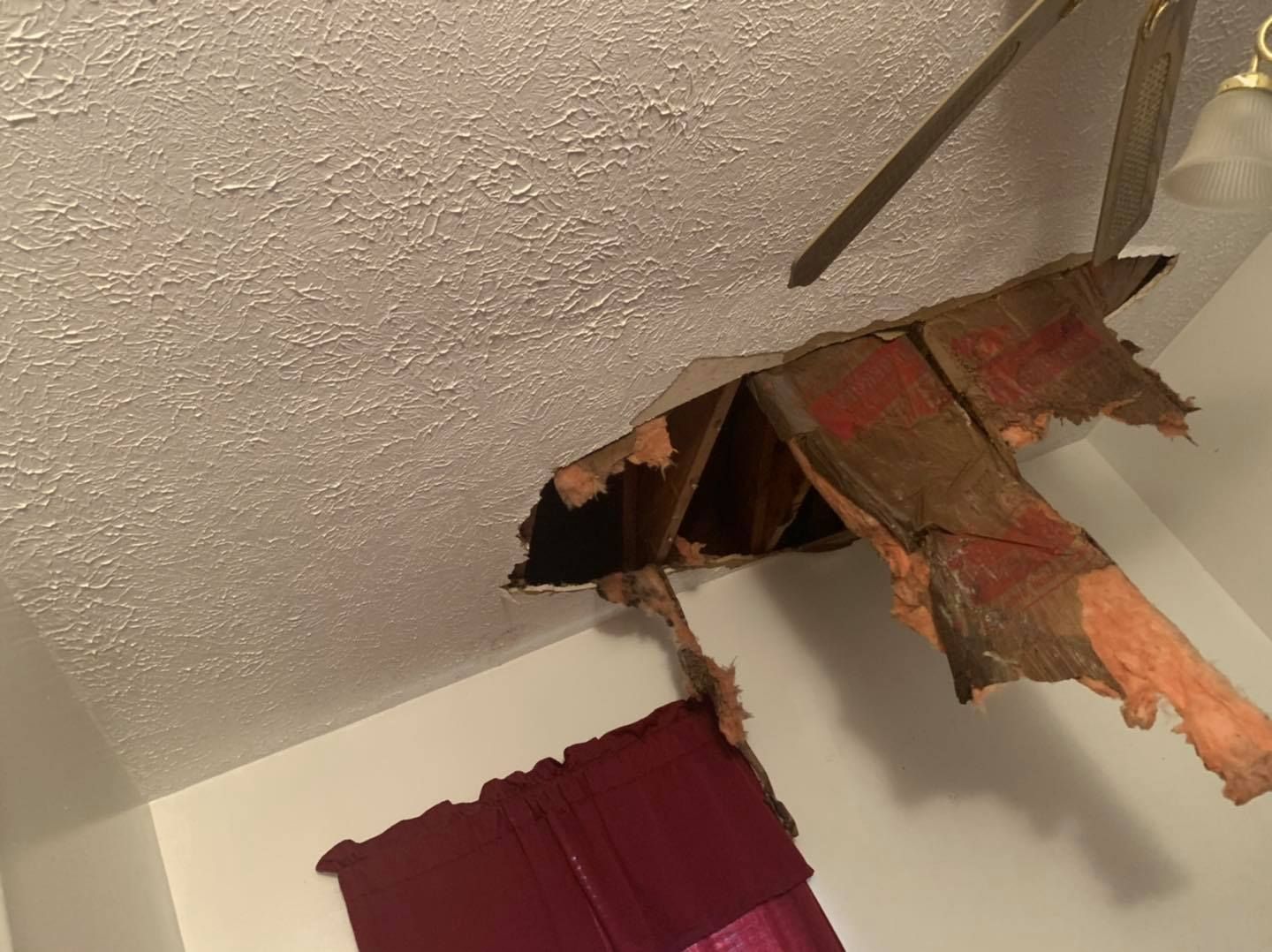 A room with a hole in the ceiling and a ceiling fan.