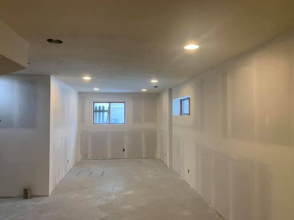A large empty room with drywall walls and a window.