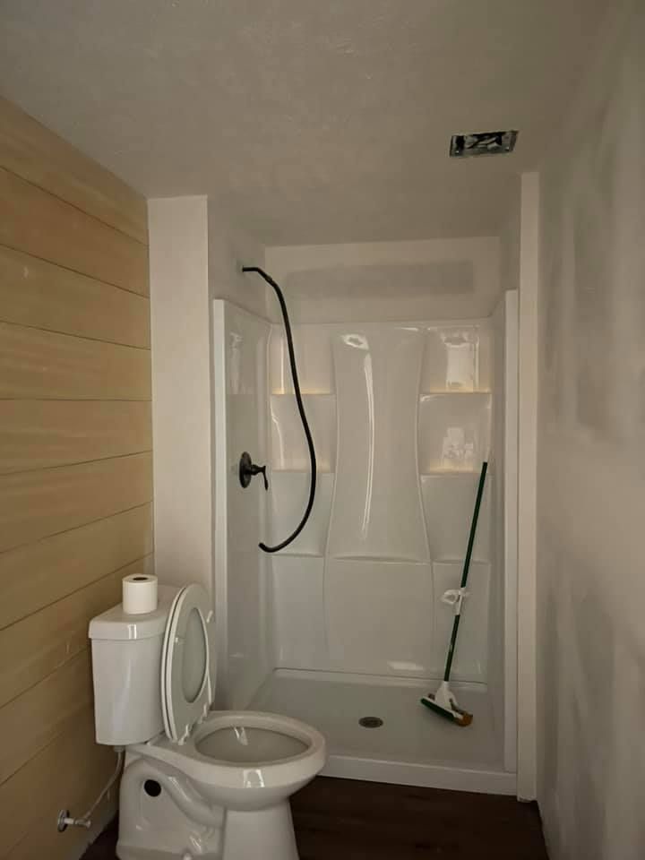 A bathroom with a toilet , shower and mop.