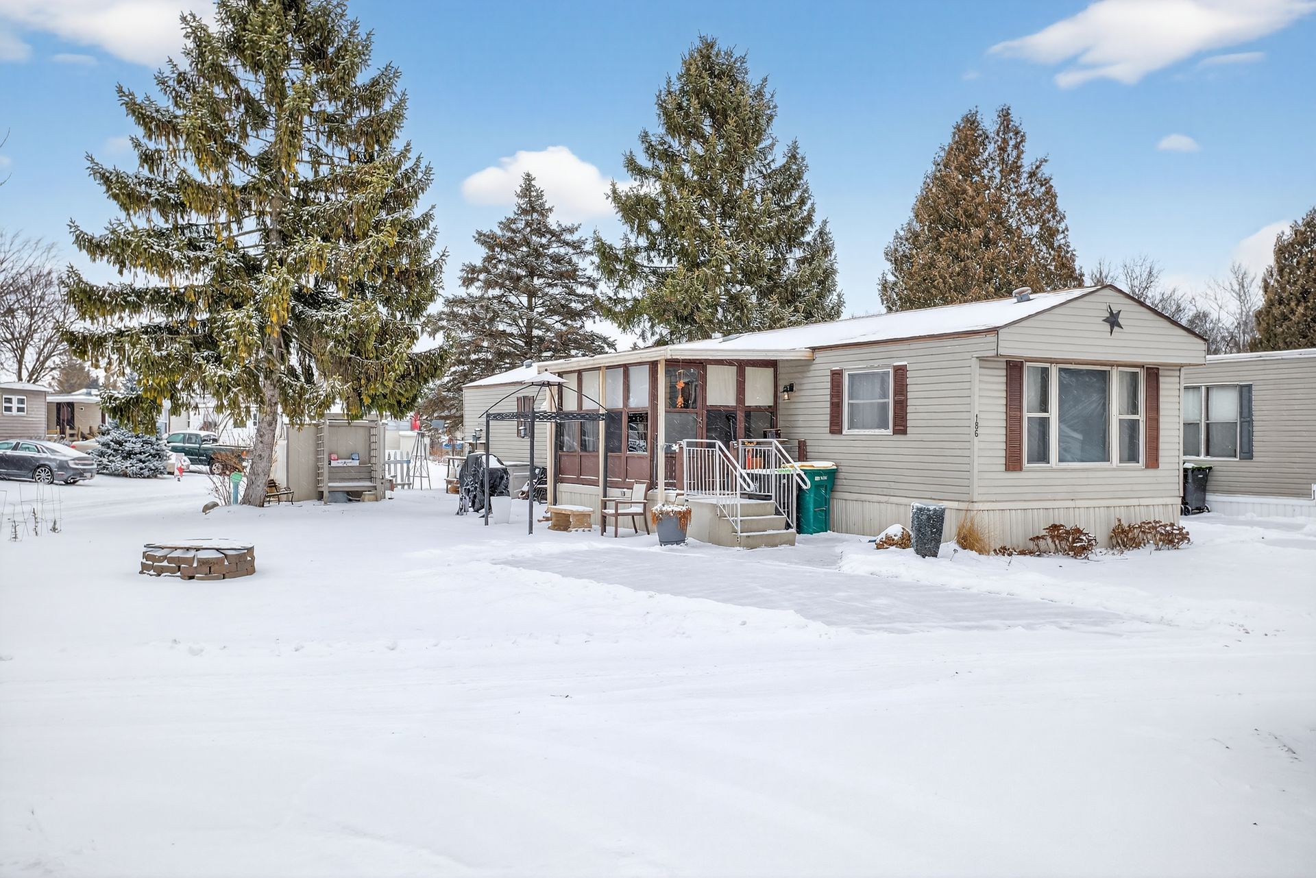Snowy, single-story home with brown shutters, a porch, and a bare yard, surrounded by trees under a blue sky.