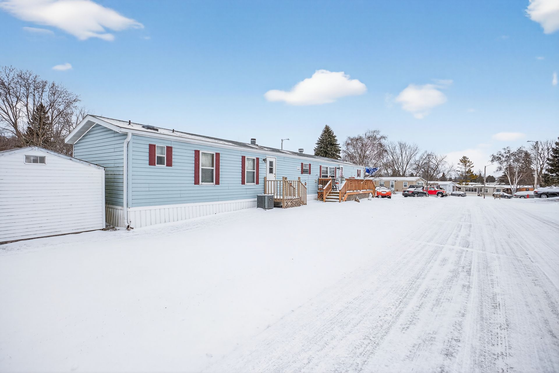 Blue mobile home with red shutters, snow-covered yard, and blue sky.