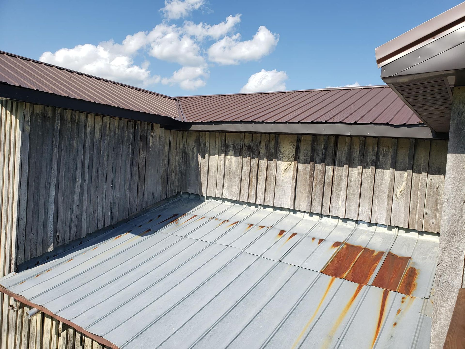 Outdoor shot of weathered wooden building with corrugated metal roof and brown metal roof. Blue sky.