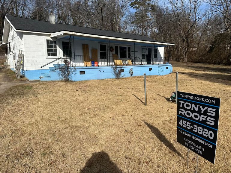 House with a blue porch and a Tony's Roofs sign on a dry, grassy lot.