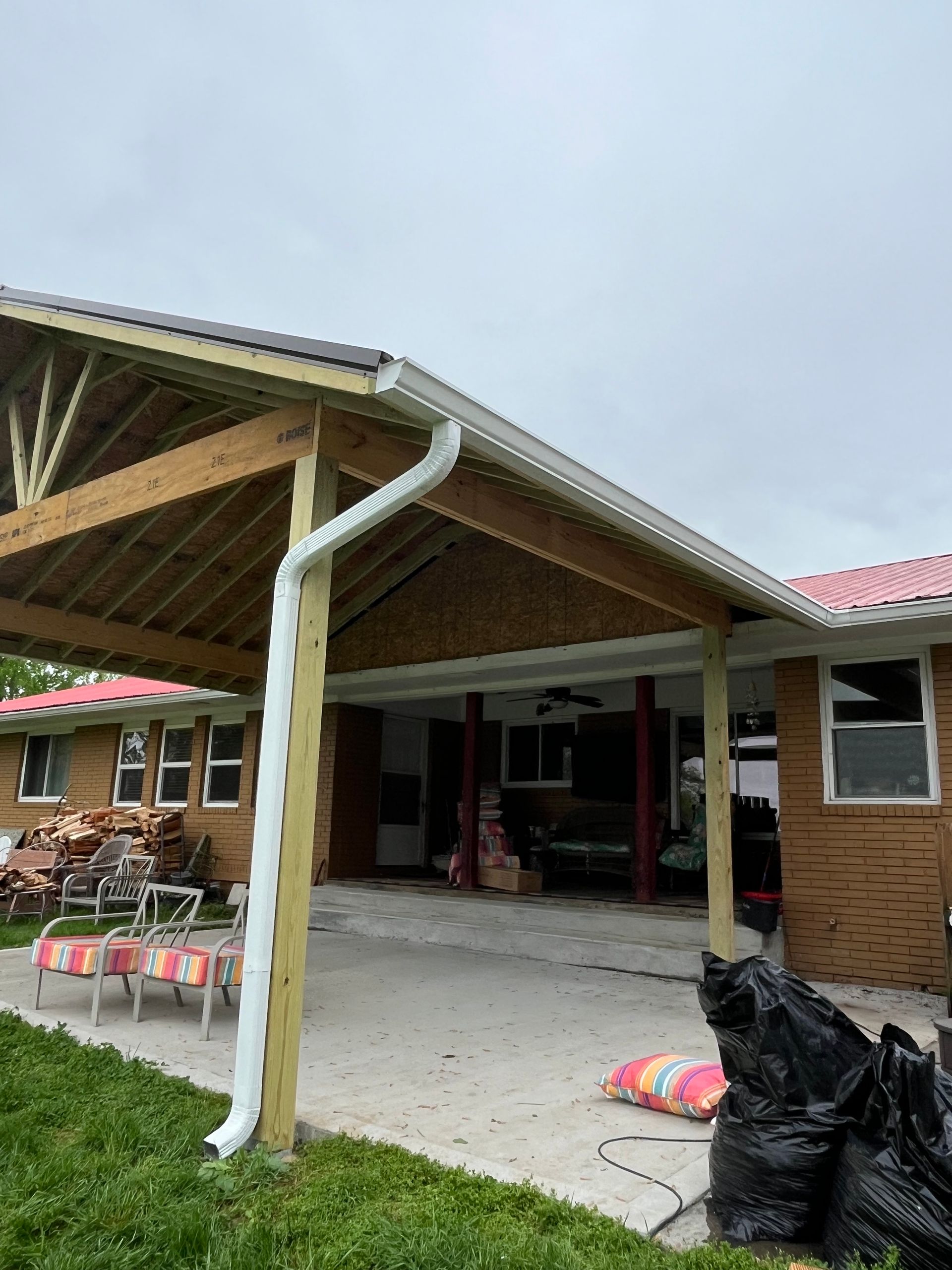 Covered patio with wooden beams and white gutter, attached to a brick home.