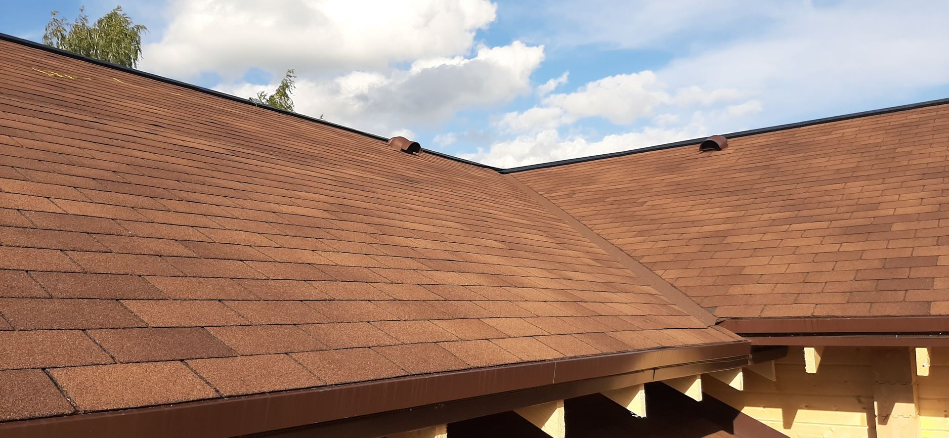 Brown shingled roof with a dark edge against a cloudy sky.
