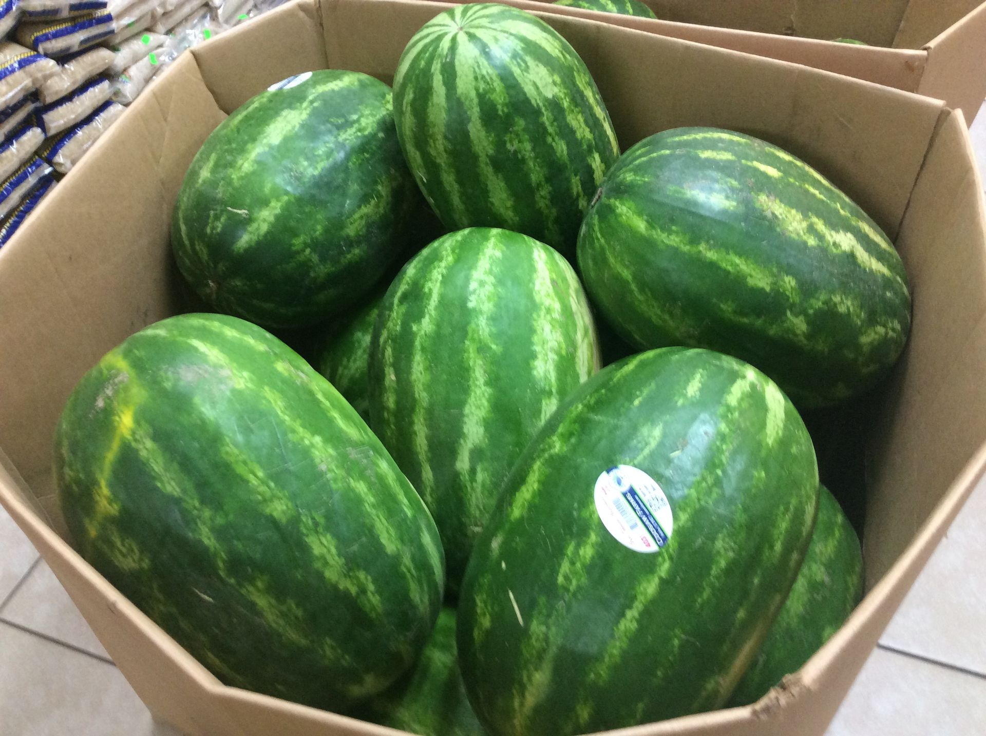 A cardboard box filled with several green striped watermelons.