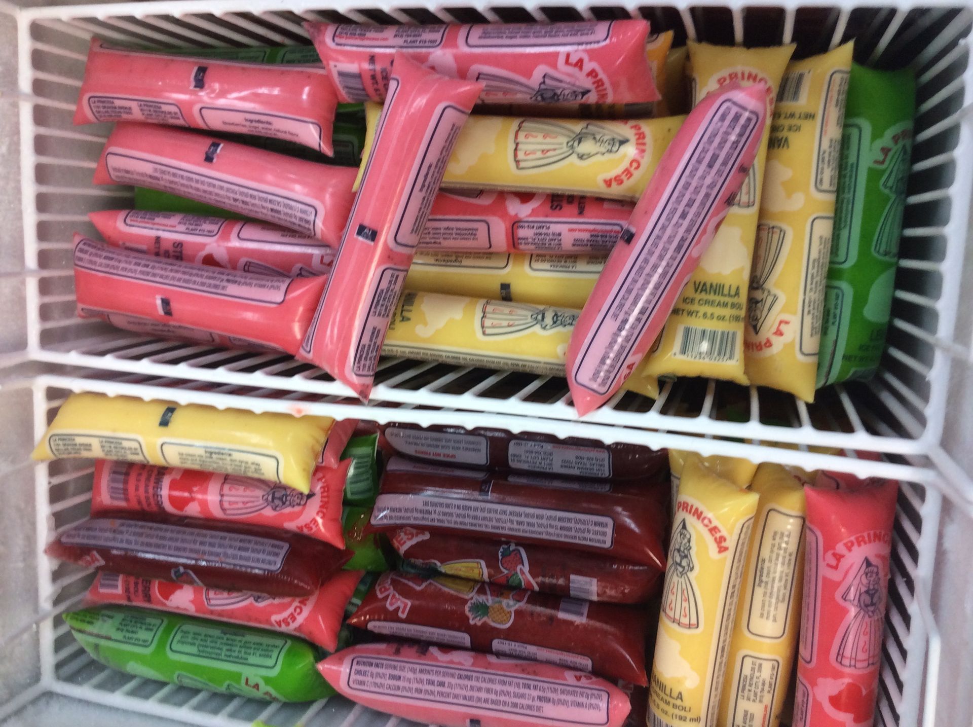 Freezer stocked with various flavors of ice pops: pink, yellow, green, and red.