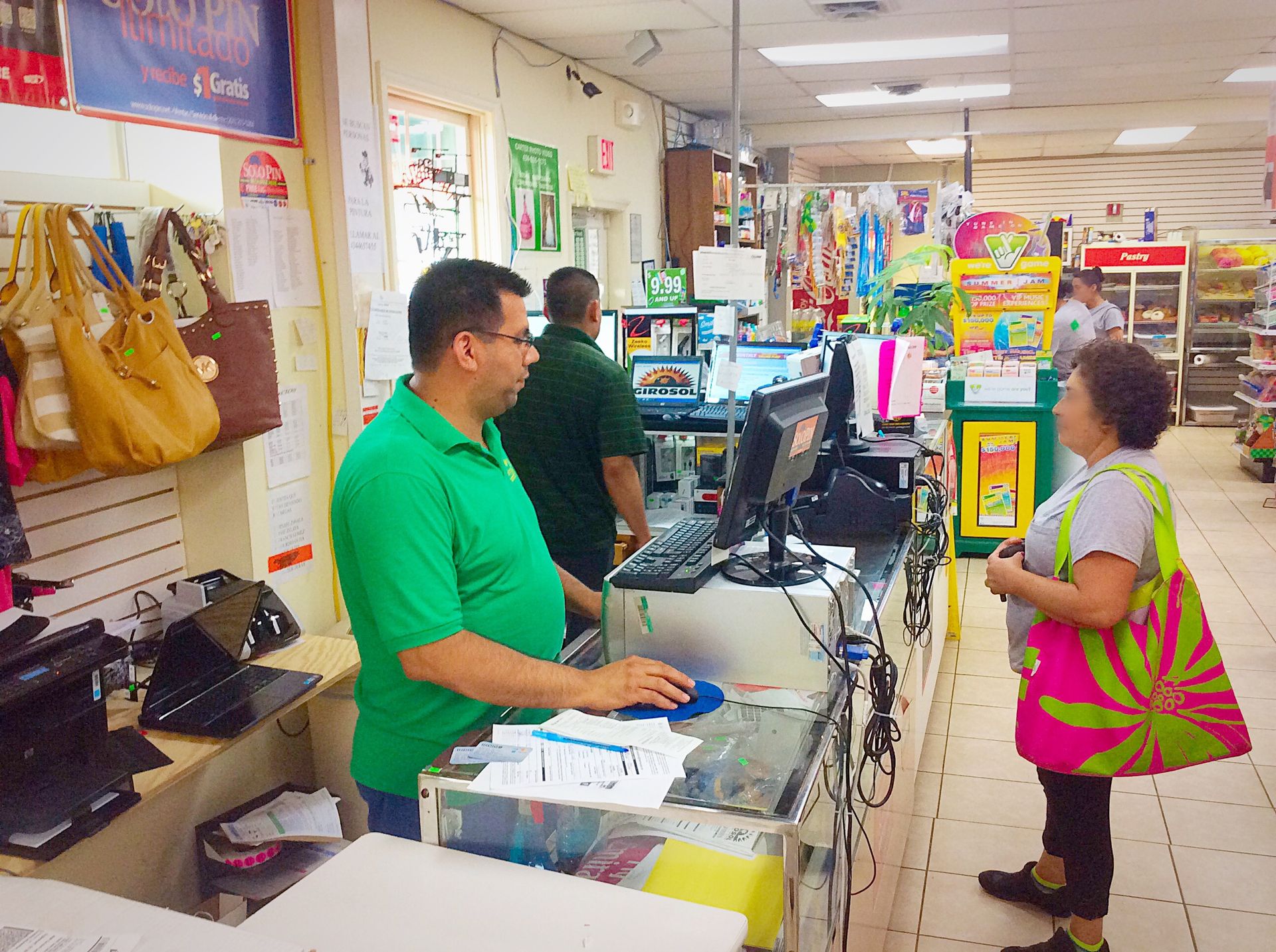 Man in green shirt rings up customer with colorful bag at a store counter.