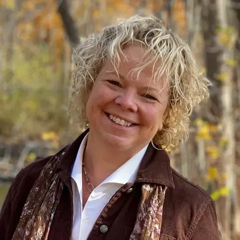 A woman in a brown jacket and scarf is smiling