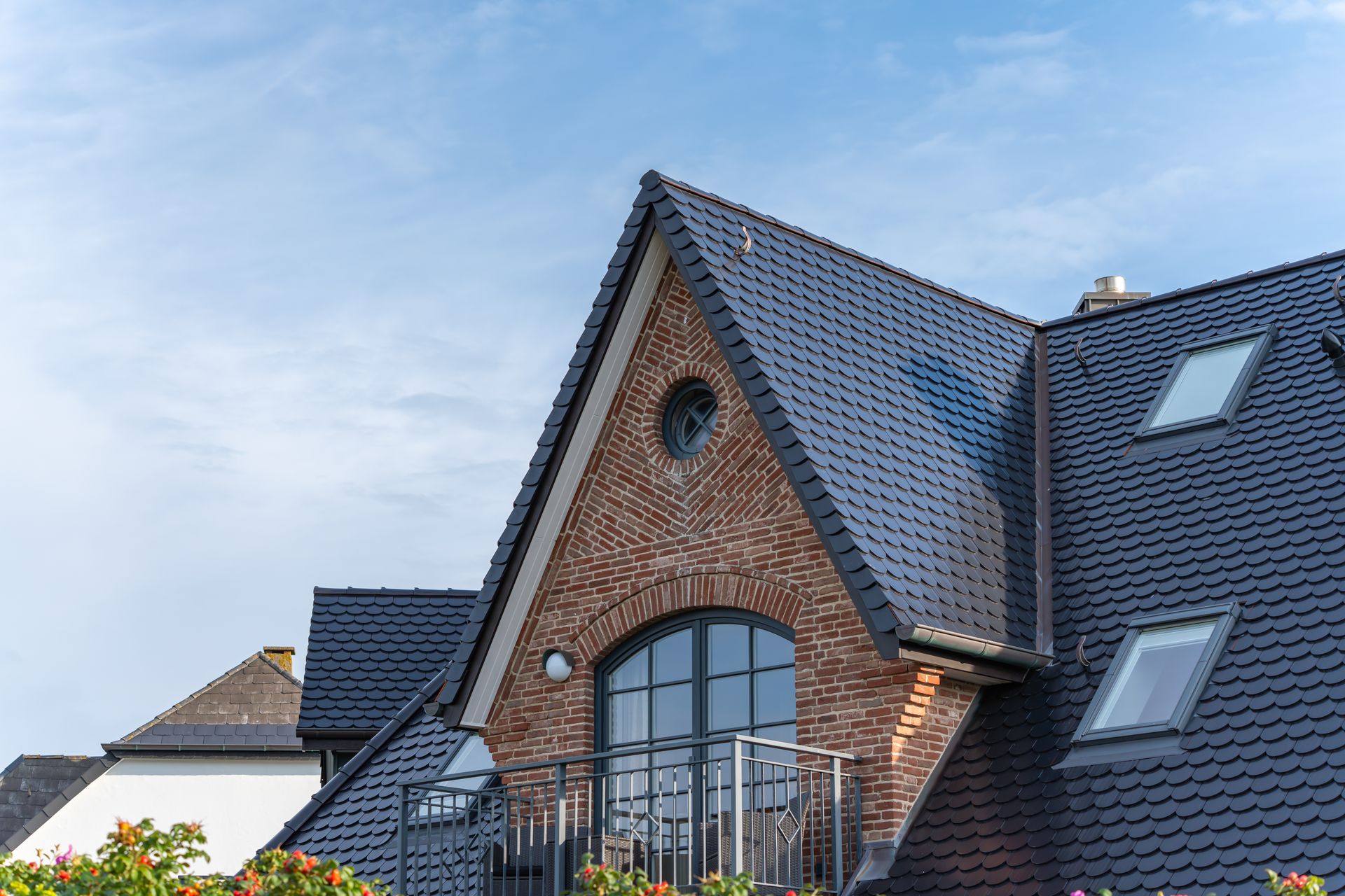 Brick house with dark gray roof, large arched window, and skylights under a blue sky
