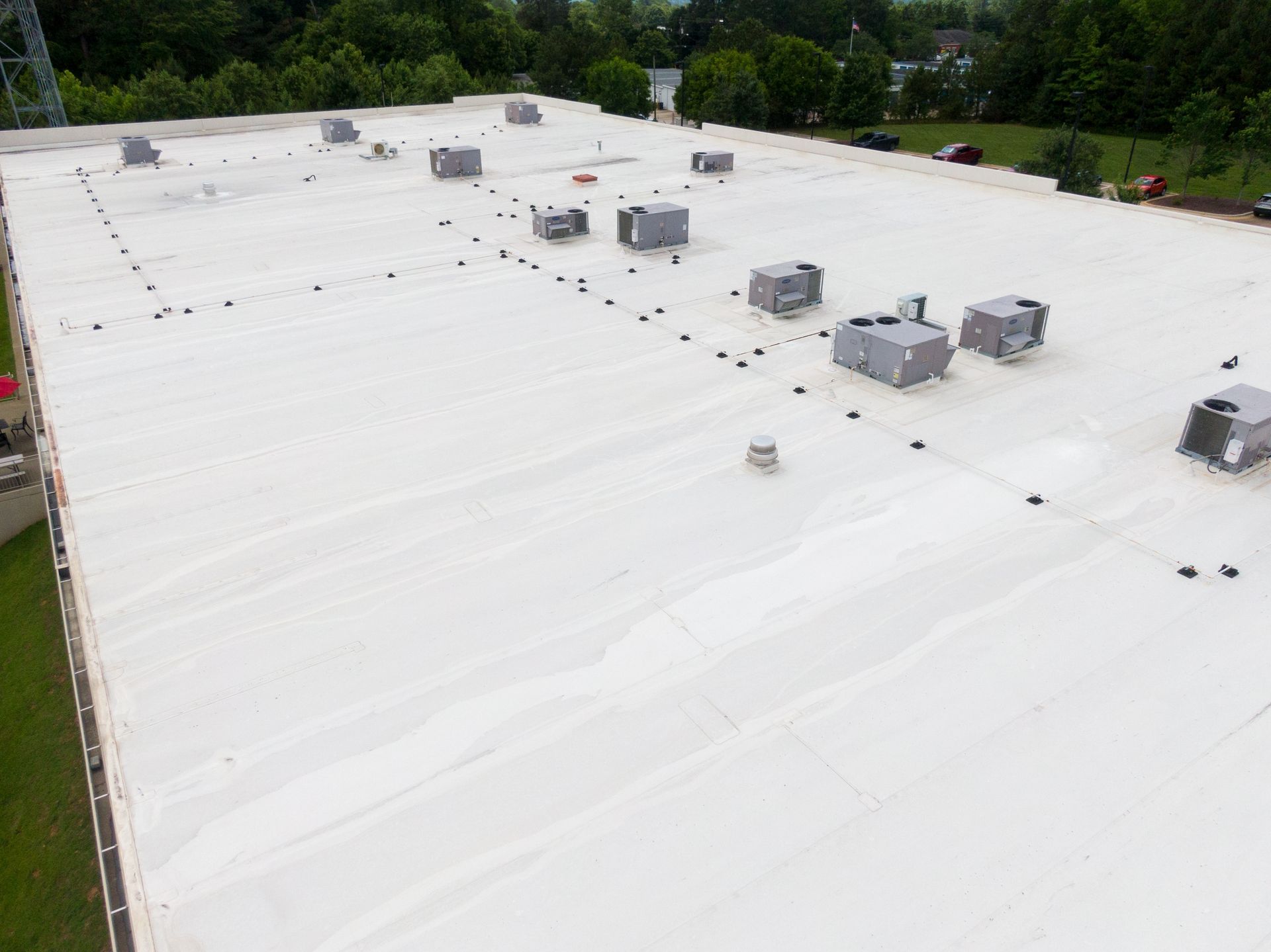 White flat rooftop with several HVAC units and surrounding trees in the background