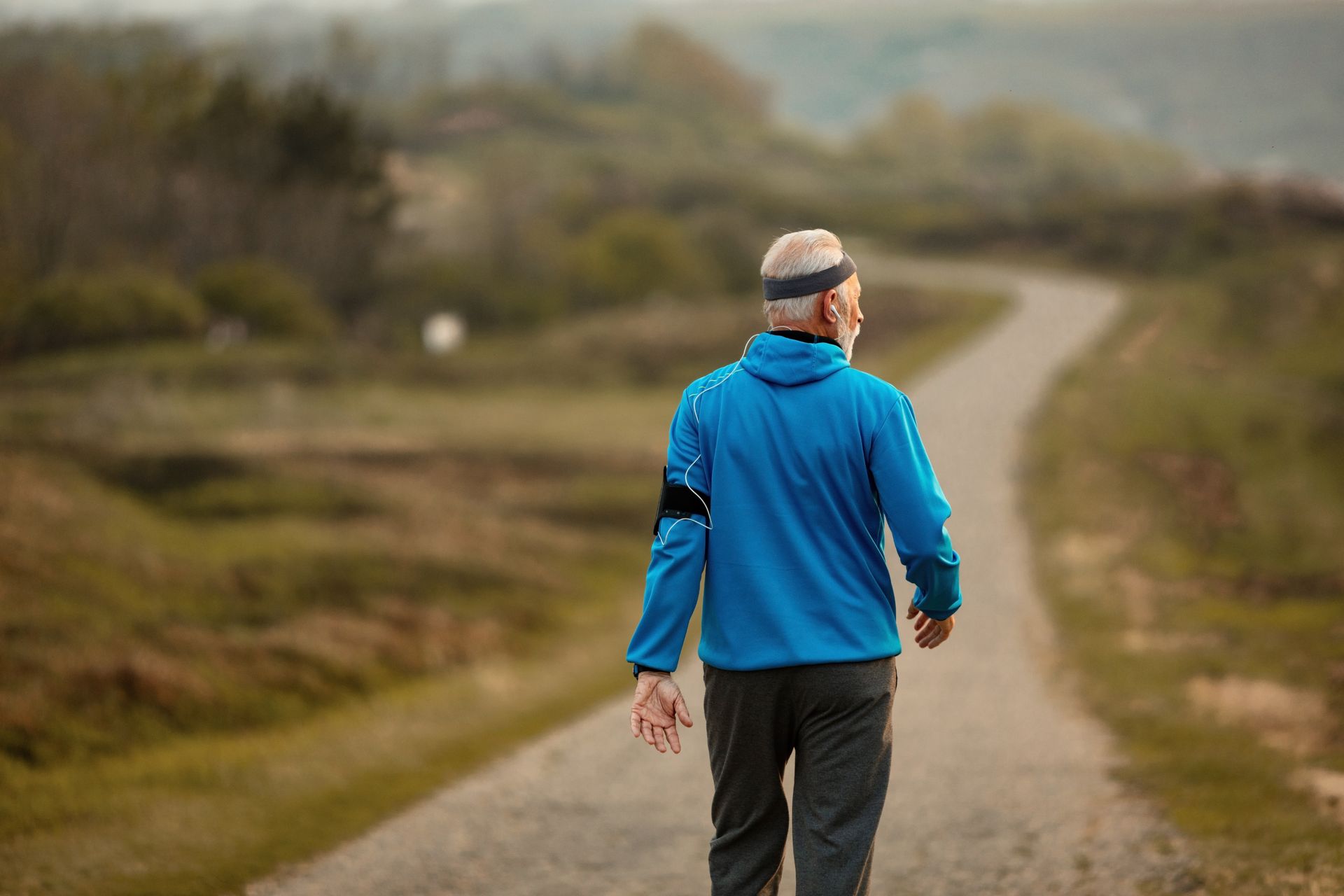 A man in a blue jacket is walking down a dirt road.