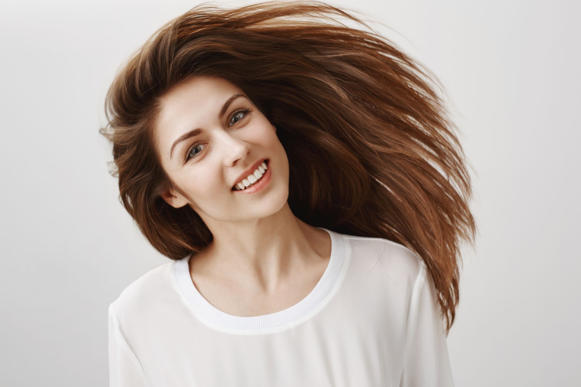 A woman with long hair is smiling with her hair blowing in the wind.