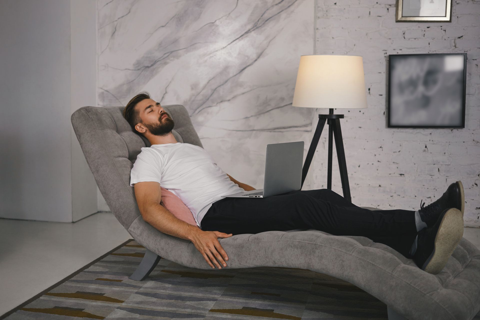 A man is laying in a chair with a laptop on his lap.