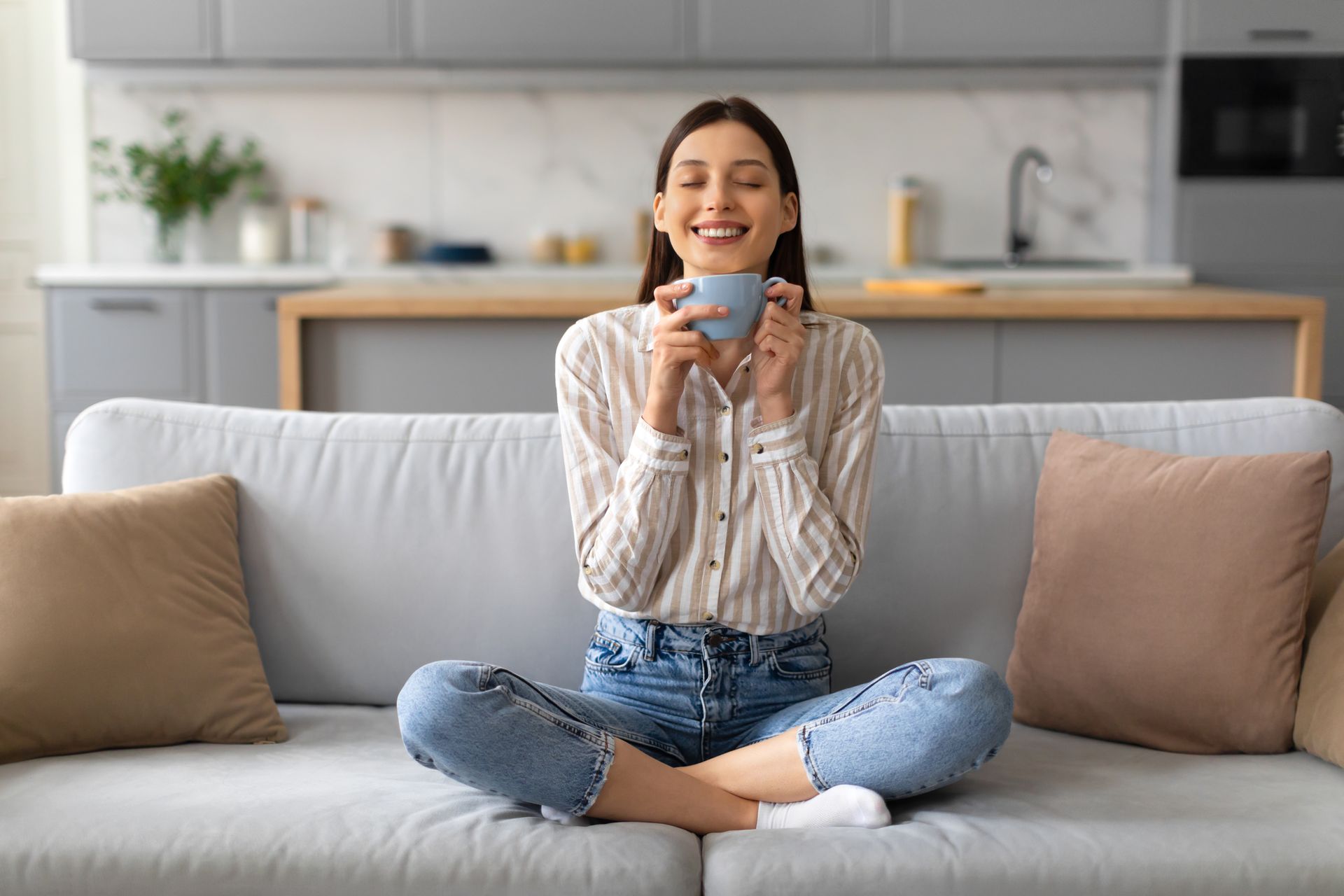 A woman is sitting on a couch drinking a cup of coffee.