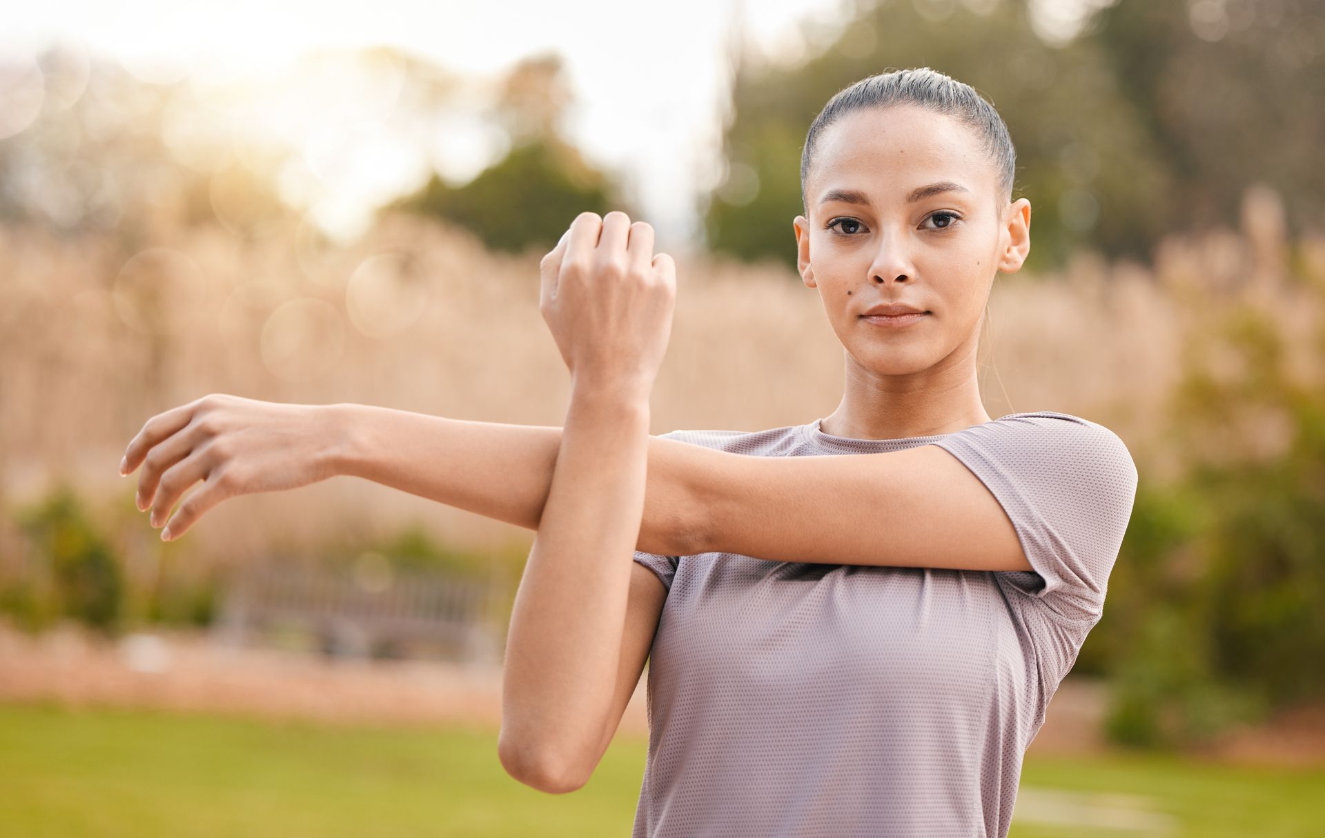 A woman is stretching her arms in a park.