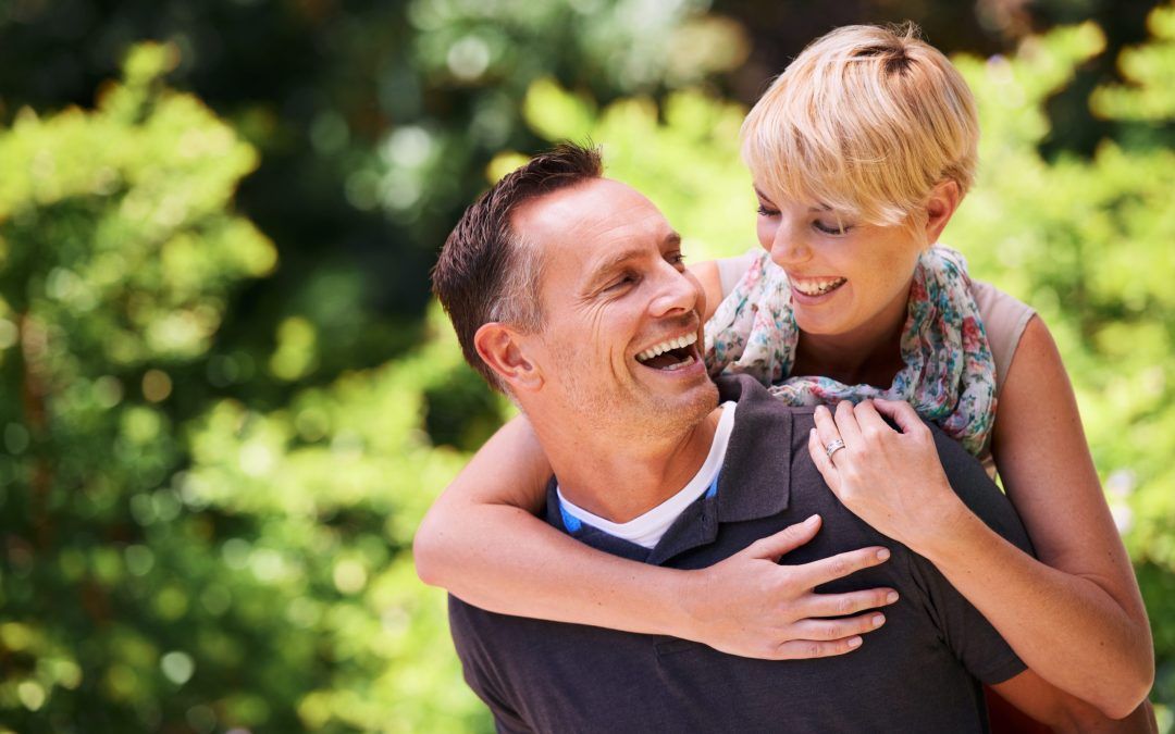 A man is carrying a woman on his back in a park.