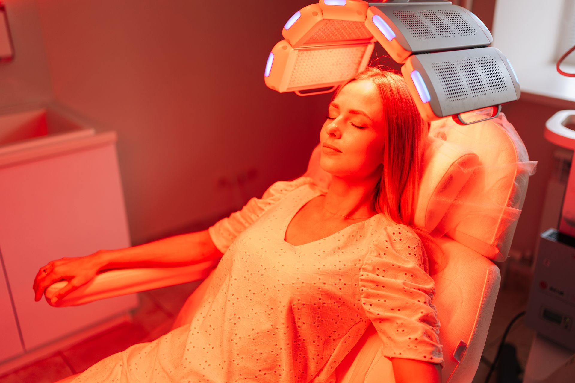 A woman is sitting in a chair with red lights on her head.