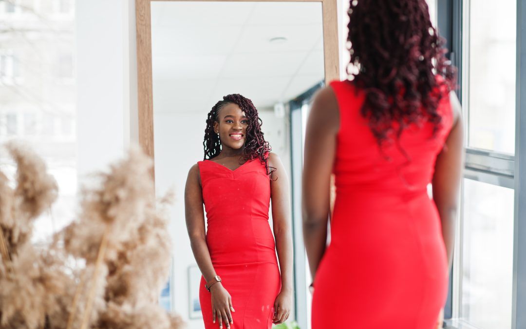 A woman in a red dress is standing in front of a mirror.