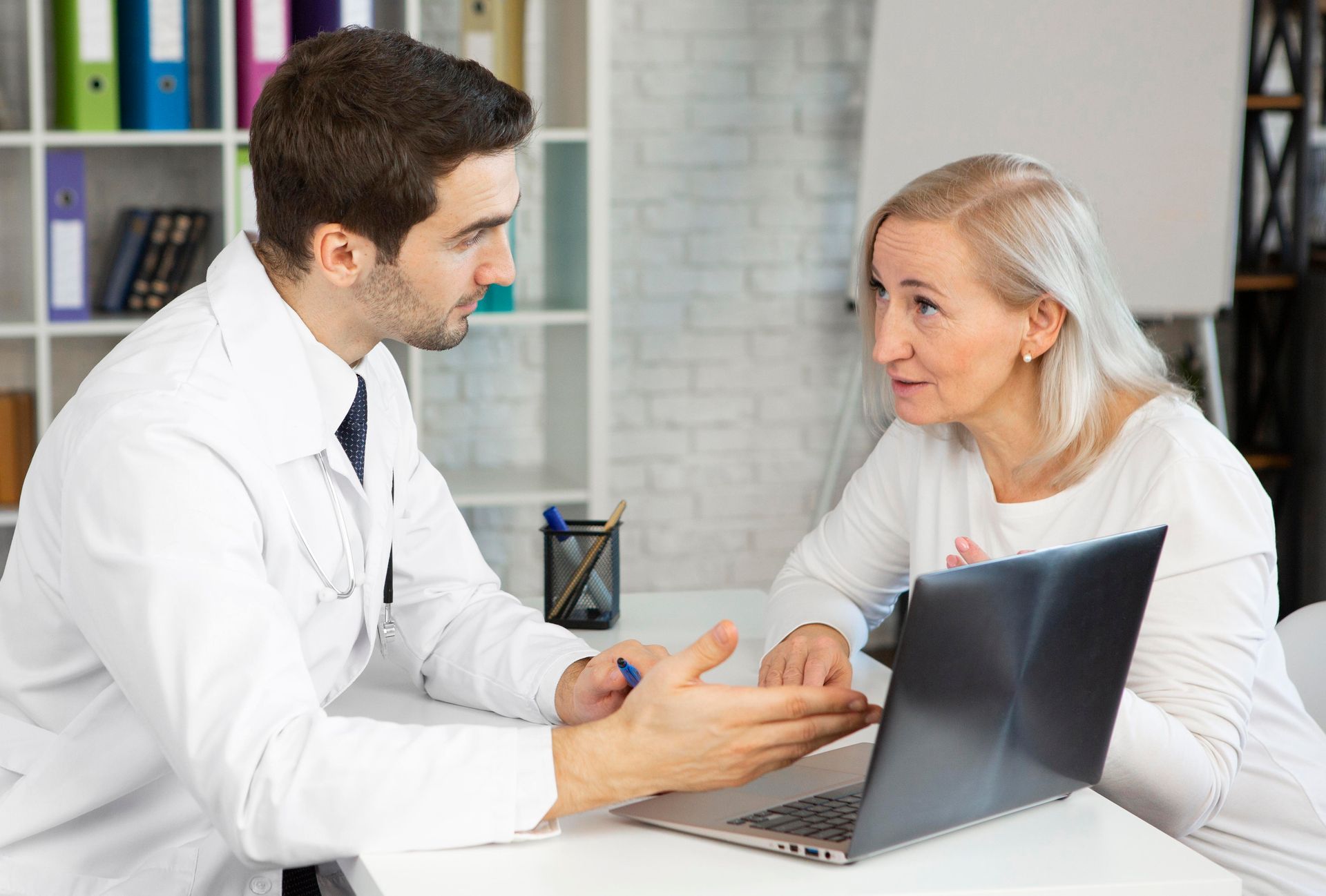 A doctor is talking to an older woman while using a laptop computer.