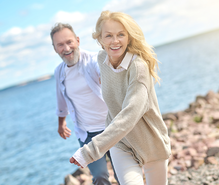 A man and a woman are walking along the shore of a lake.